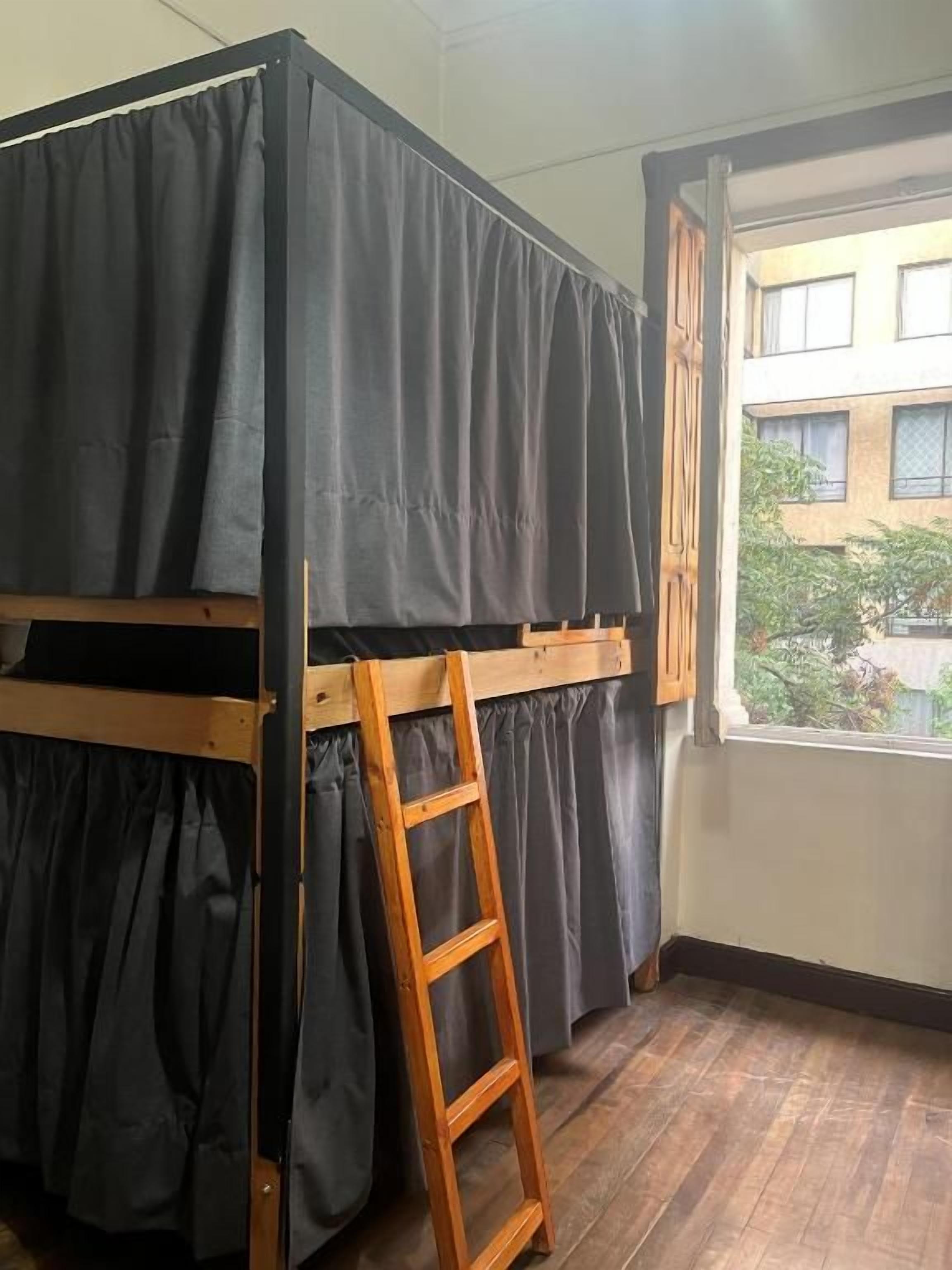 Una cama litera con escalera, una ventana con cortinas y vistas de edificios.