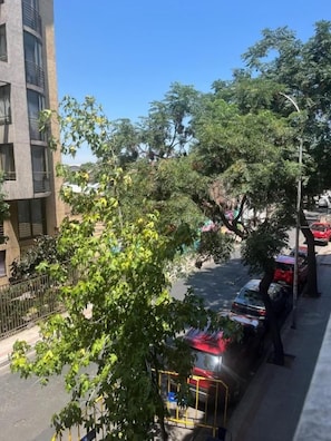 Vista de la calle con un edificio a la izquierda, árboles y coches aparcados.