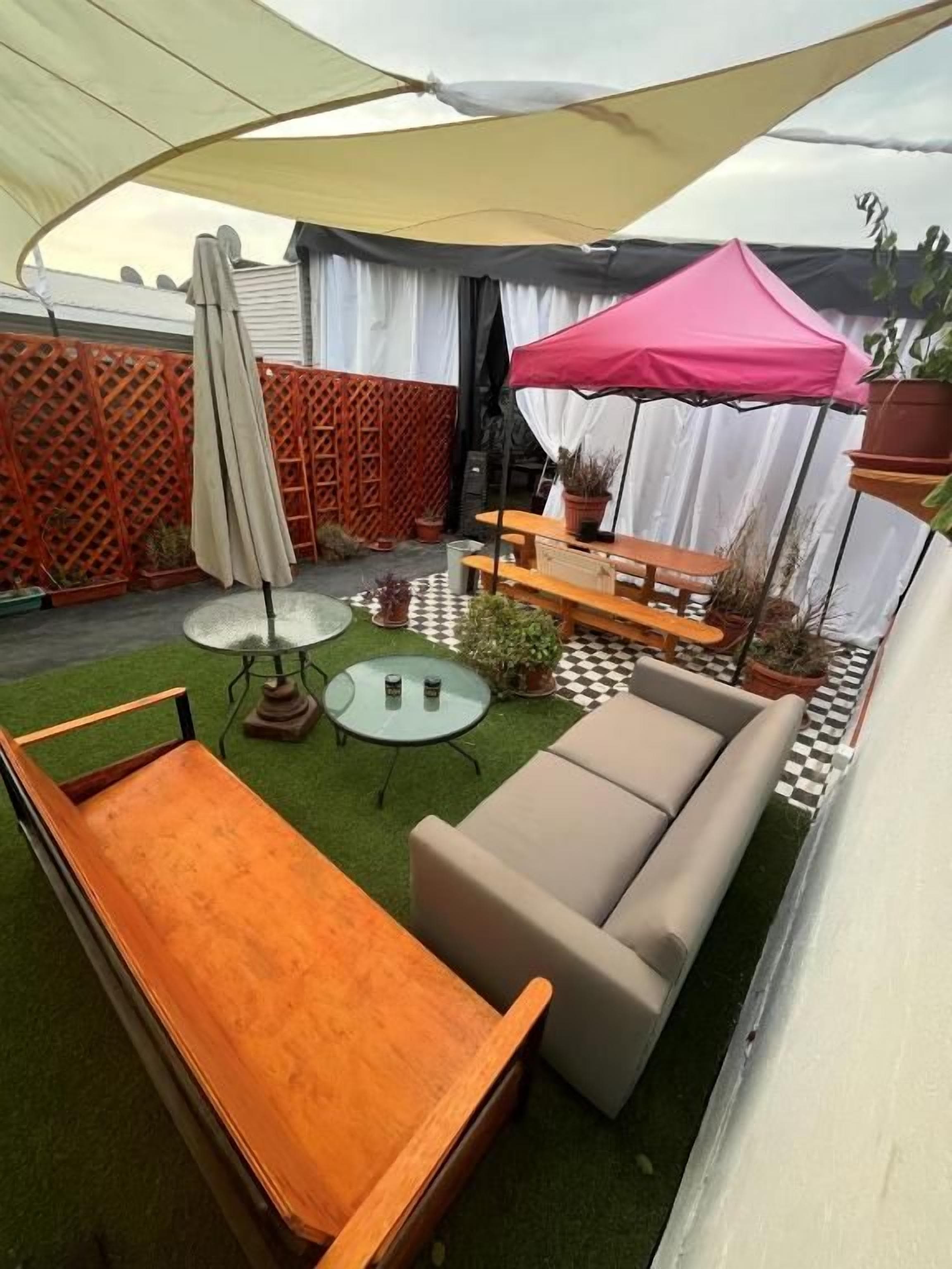 Un patio con una mesa de madera, un sofá y un paraguas rosa.