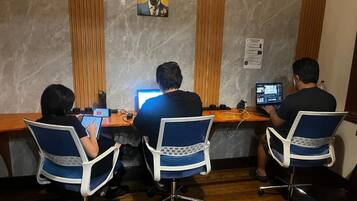 Tres personas sentadas en un escritorio de madera con computadoras, en una habitación con pared de mármol y una obra de arte con motivos de cebra.