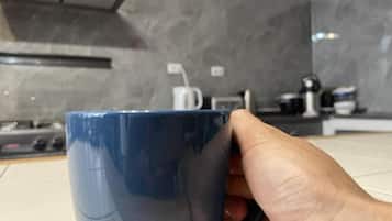 Una mano sosteniendo una taza azul en una cocina de diseño moderno, con una estufa y una cafetera.
