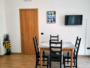 A dining area with a wooden door, a table with chairs, a wall-mounted TV, and a photo collage.