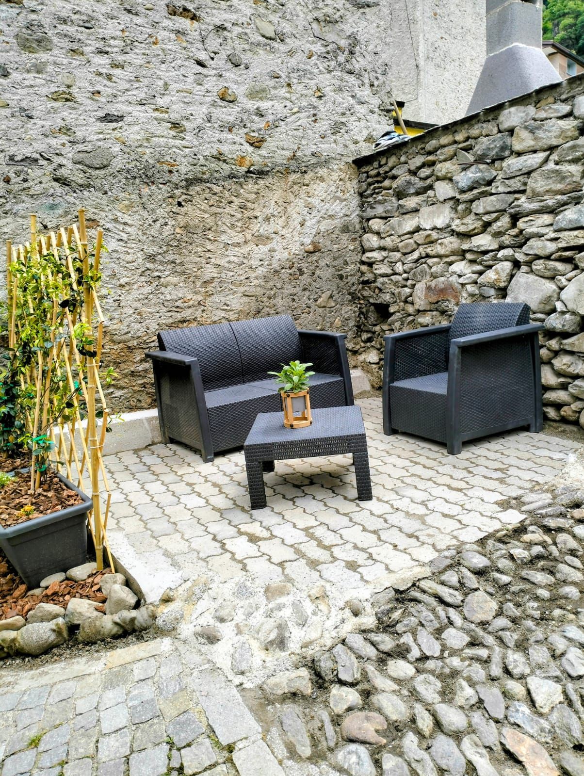 Ein Sitzbereich im Freien mit einer Steinwand, einem kleinen Tisch und zwei Stühlen.