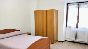 A bedroom with a wooden bed, a wardrobe, and a window with curtains. - Vrbo Property (Forcola)