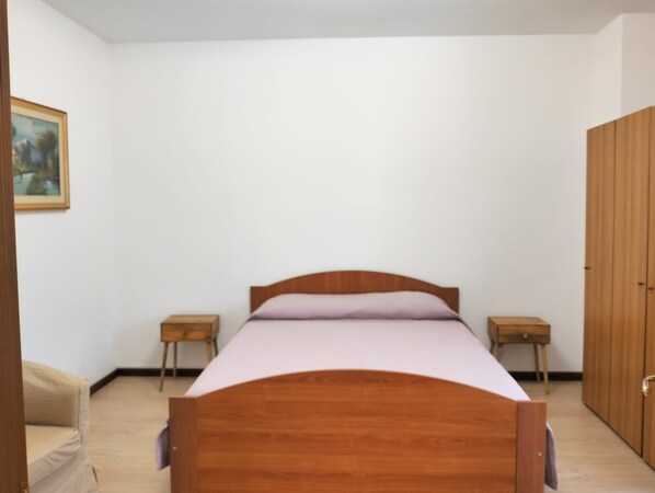 A bedroom with a wooden bed, two bedside tables, a wardrobe, and a framed picture on the wall.