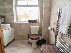 A compact bathroom with a toilet, sink, and a window. - Hafan Deg (Holywell)