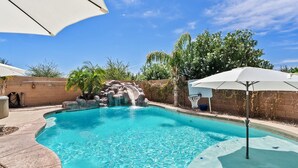 Une piscine agrémentée d’une cascade, entourée d’un mur de briques et de palmiers.