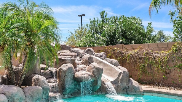 Une piscine avec une cascade artificielle en roches et des palmiers.