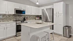 Une cuisine moderne avec des meubles blancs, des appareils en acier inoxydable, un pare-feu en carrelage et des luminaires suspendus.