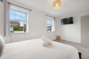 Une chambre moderne avec un grand lit, un téléviseur à écran plat fixé au mur et une fenêtre donnant sur l’extérieur.