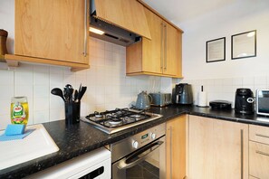 A kitchen with wooden cabinets, a gas stove, a coffee maker, and a toaster. - Serene 2BR House | Garden & Parking | Stay With Us (Stockton-on-Tees)
