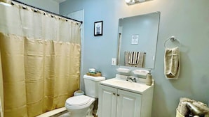 A bathroom with a shower curtain, toilet, sink, and a towel rack.