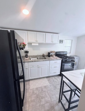 A kitchen with white cabinets, a black refrigerator, a stove, and a sink.