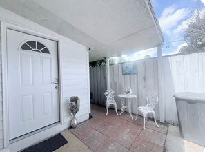 A covered porch with a white door, a small table, and two chairs.