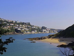 A coastal town with houses on a hillside, a sandy beach, and calm water. - Beachstone (Salcombe)
