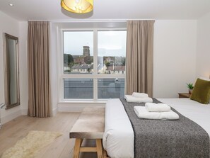 A hotel room with a large window, a bed with white linens, a bench, and a small table with a plant. - Beachstone (Salcombe)