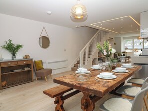 A dining area with a wooden table set for four, a staircase, and a view of the outside. - Beachstone (Salcombe)