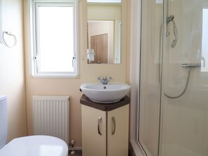 Ein Badezimmer mit einem weißen Waschbecken, einem Spiegel, einer Dusche und einem Fenster.