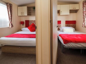 Ein Schlafzimmer mit zwei Betten, jeweils mit roter Decke und Kissen, und Holzboden.
