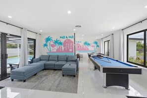 Ein modernes Wohnzimmer mit Billardtisch und einem großen, grauen Ecksofa.