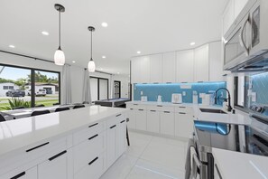 A modern kitchen with white cabinetry, a central island, pendant lighting, and a view of the outside. - Miami Gardens Oasis - Private Pool & Pool Table (Miami Gardens)