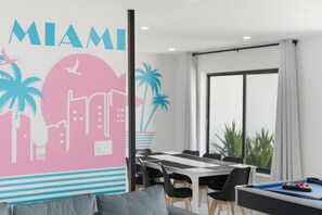 A modern hotel room with a cityscape mural, a dining area with a pool table, and a large window offering a view of the outdoors. - Miami Gardens Oasis - Private Pool & Pool Table (Miami Gardens)
