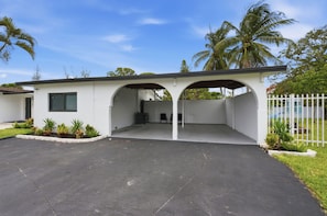 A modern building with a covered parking area, a small garden, and a white fence.
