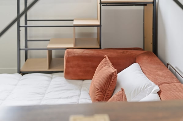 A bed with a white mattress and two pillows, one white and one brown, in a room with a metal bunk bed structure in the background.
