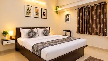 Quarto de hotel com uma cama grande, mesa de cabeceira com abajur, uma cadeira pequena, planta em vaso e uma janela com cortinas.