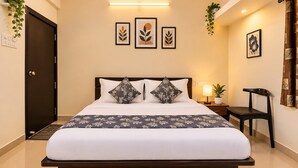 Une chambre d’hôtel comprenant un lit, une table de chevet, une lampe, une chaise et des œuvres d’art accrochées aux murs.