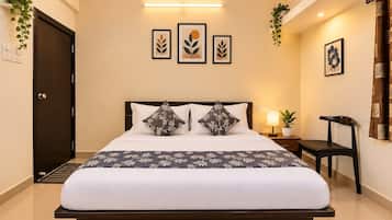 Quarto de hotel com cama, mesa de cabeceira, abajur, cadeira e obras de arte nas paredes.