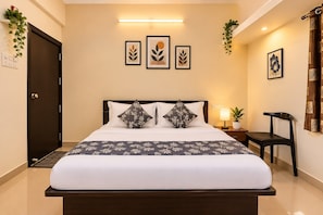 Ein Hotelzimmer mit Bett, Nachttisch, Lampe, Sessel und Kunstwerken an den Wänden.
