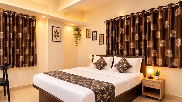 Une chambre moderne avec un grand lit, des rideaux foncés ornés de motifs de feuilles, une table de chevet avec une lampe et une petite plante.