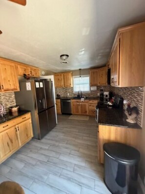 A kitchen with wooden cabinets, a refrigerator, a dishwasher, and a granite countertop.