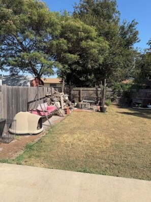 A backyard with a fenced area, a tree, and a small structure.