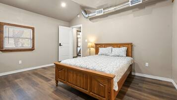 Un dormitorio con cama de madera, ventana con persianas, puerta y rejilla en el techo.