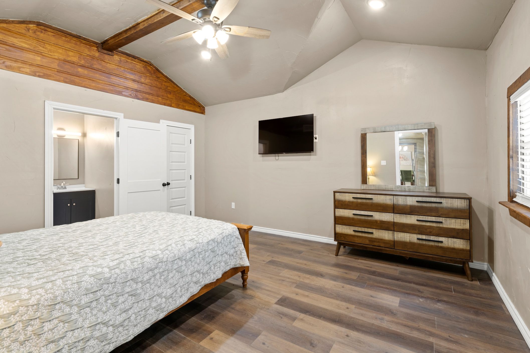 A bedroom with a bed, dresser, TV, and ceiling fan.