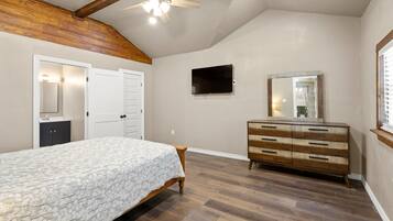 A bedroom with a bed, dresser, TV, and ceiling fan.