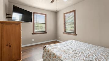 A bedroom with a bed, a wooden wardrobe, a ceiling fan, and two windows with blinds.