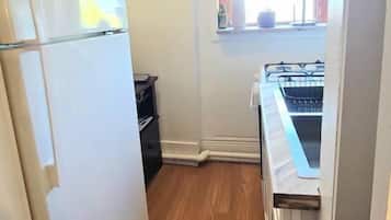 Cozinha compacta com geladeira, fogão e janela com cortinas.
