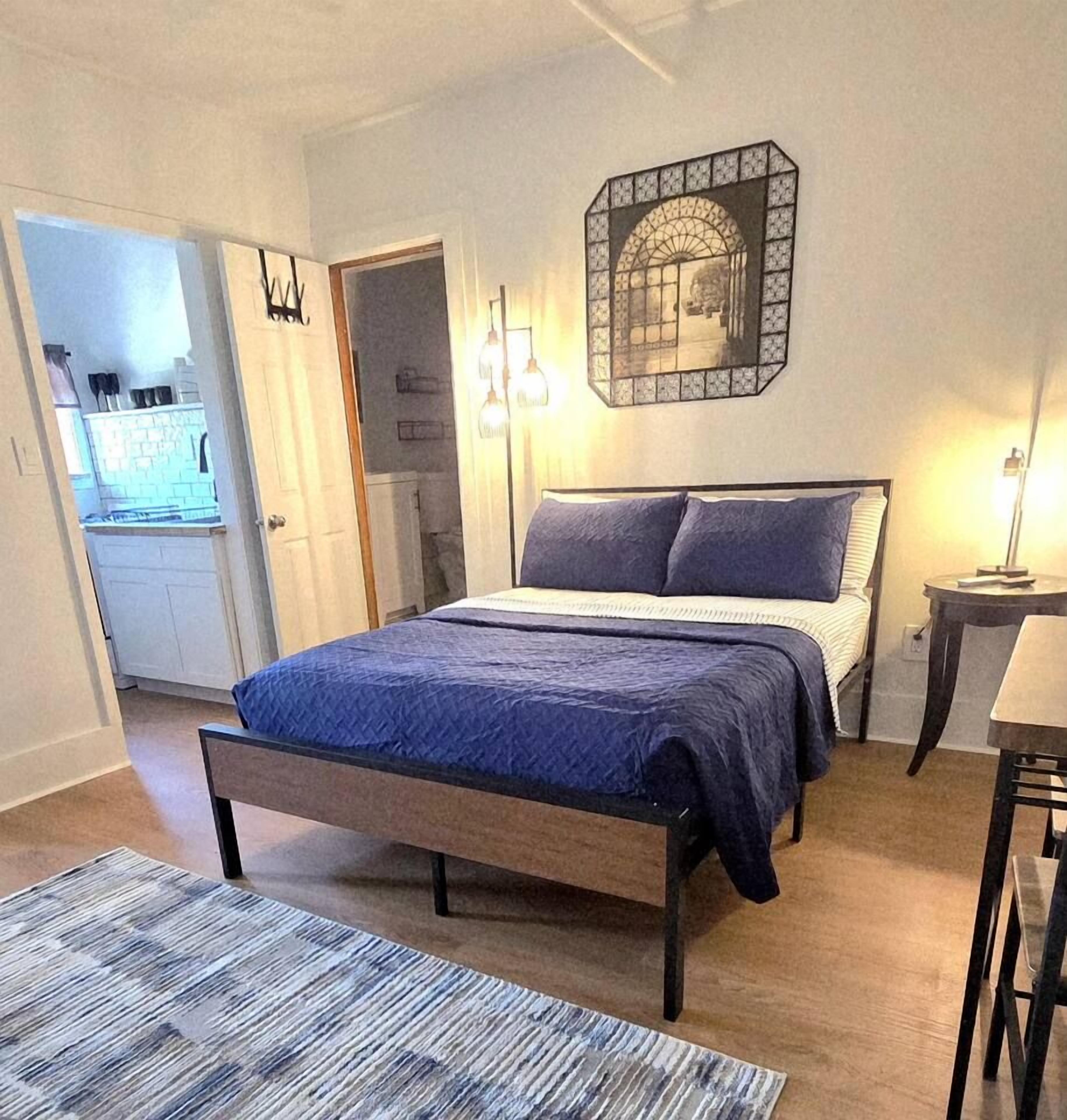 Quarto com cama, mesa de cabeceira e luminária na parede.