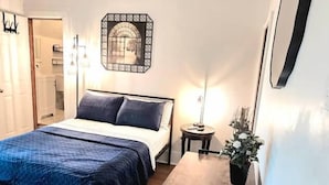 A bedroom with a bed, bedside table, lamp, and a wall-mounted mirror. - The Tidy Third Floor Studio (Buffalo)