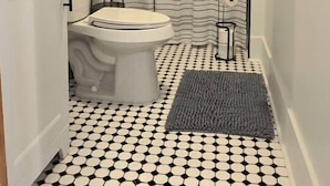 A bathroom with a white toilet, a shower with a black towel, and a patterned floor. - The Tidy Third Floor Studio (Buffalo)