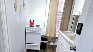 A narrow hallway with a white stove, a trash bin, and a door leading to a room. - Cozy Studio in Allentown (Buffalo)