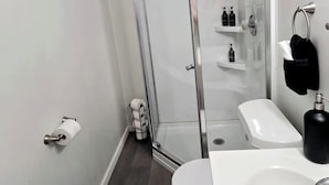 A modern bathroom with a glass shower enclosure, a white toilet, and a sink with a black soap dispenser. - Cozy Studio in Allentown (Buffalo)