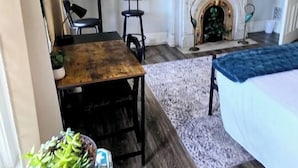 A hotel room with a fireplace, a television mounted above it, a bed with a blue bedspread, a small table with a plant, and a patterned rug. - Cozy Studio in Allentown (Buffalo)