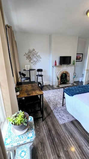 Ein Hotelzimmer mit Kamin, einem darüber montierten Fernseher, einem Bett mit blauer Bettdecke, einem kleinen Tisch mit Pflanze und einem gemusterten Teppich.