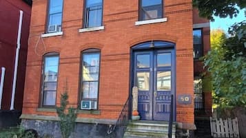 Un edificio de ladrillo de dos pisos con una puerta principal, unos pocos escalones y el número '50' en la pared.
