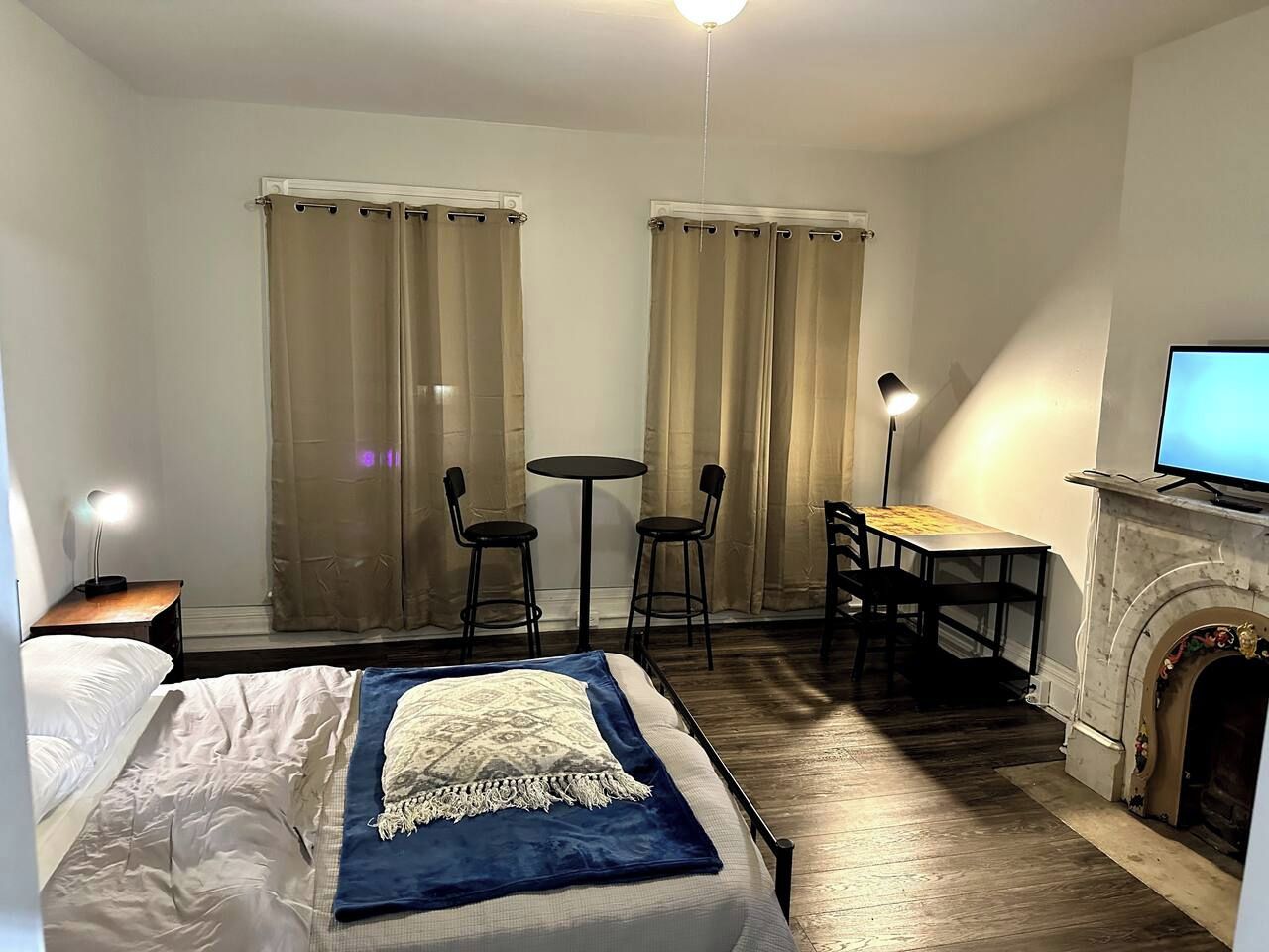 A hotel room with a bed, a desk, two chairs, a television, and a fireplace.