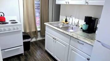 Una cocina compacta con armarios blancos, estufa, fregadero y cafetera.